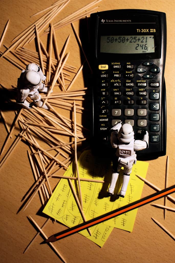 Zahnstocher, Post its, Taschenrechner, Astronauten und Bleistift auf einem Schreibtisch.
